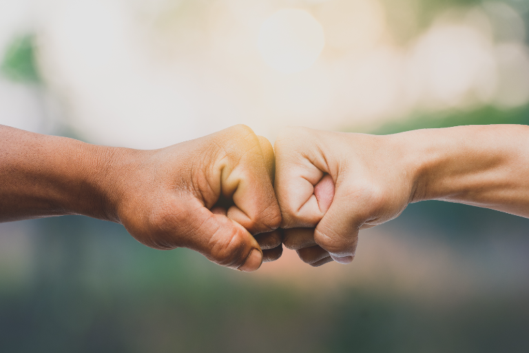 Two people fist-bumping in a warm sunlit setting