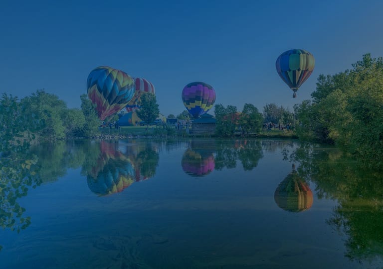 Hot air balloons rising over Windsor Lake at sunrise during the Windsor Balloon Festival